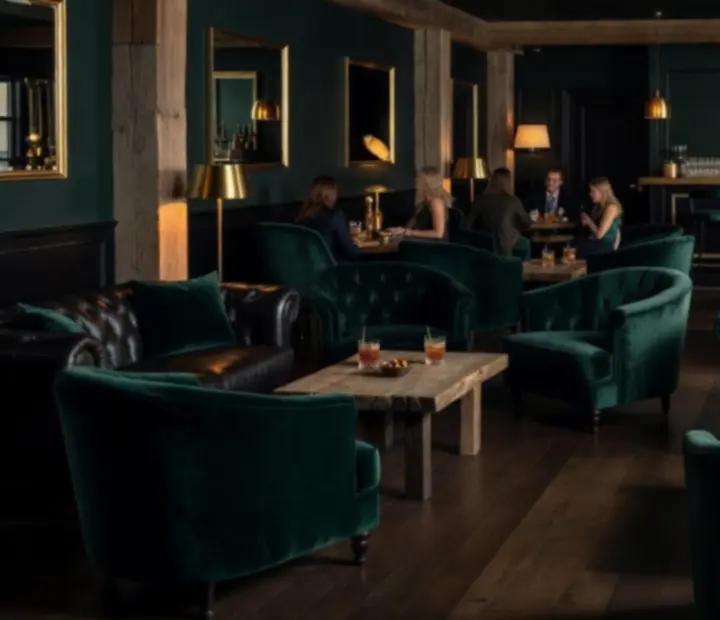Intimate jade-toned bar with raw timber shelving, gold detailing, and plush lounge seating